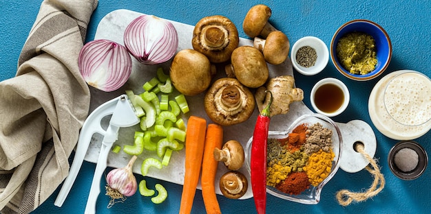 Banner di ingredienti per cucinare il curry indiano di verdure, zucche e funghi su sfondo blu e spezie riprese dall'alto dello spazio di copia