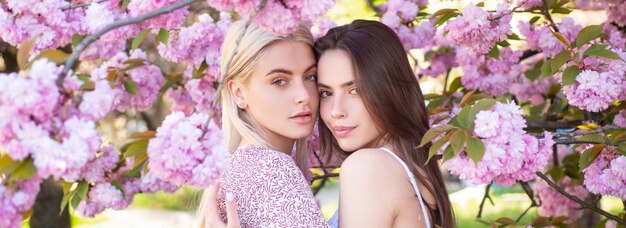 Banner di primavera con amiche donne all'aperto due giovani donne sexy sensuali che si rilassano nei fiori di sakura