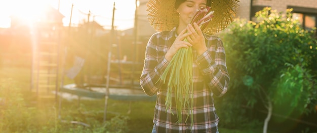 Banner giardiniere femminile annusa mazzo di cipolle verdi nella soleggiata giornata di primavera calda copia spazio Cura delle piante e concetto di raccolta e hobby