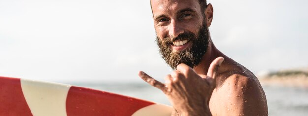 Banner orizzontale o intestazione con surfista felice con surf surf sorridente facendo mano shaka hawaiana o appendere un cartello sciolto per divertimento durante la sessione di surf nelle onde dell'oceano in vacanza al mare