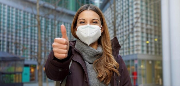 Banner panoramico vista ritagliata di pollici in su donna che indossa maschera protettiva e abiti invernali in città