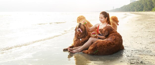 Banner size photo Giovane donna seduta e giocare con i suoi cani sulla spiaggia al tramonto Rilassamento con un animale domestico