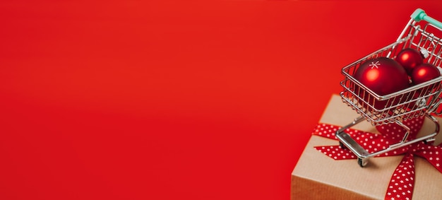 Banner web per lo shopping di saldi natalizi con carrello mini carrello con confezione regalo e palline rosse per ornamenti natalizi