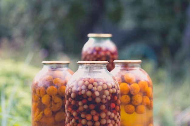 Barattoli con composta sul tavolo Barattoli di vetro sigillati con kompot posti sul tavolo vicino a fiori e frutti nelle giornate estive in giardino