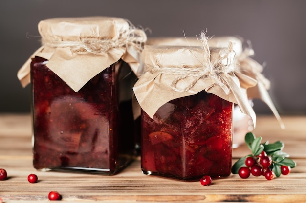 Barattoli di marmellata di mirtilli rossi e pere fatti in casa con carta artigianale sui coperchi sul tavolo di legno accanto ai mirtilli rossi freschi