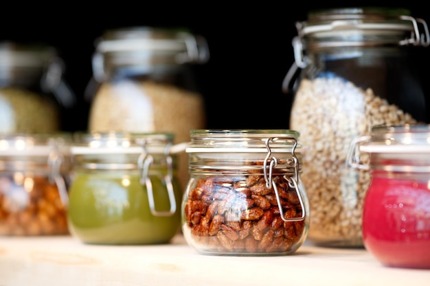 Barattoli di vetro con marmellata di burro di noci di grano sullo scaffale di legno sullo sfondo di una parete scura concetto di colazione sfondo cucina mangiare sano concetto concetto di conservazione