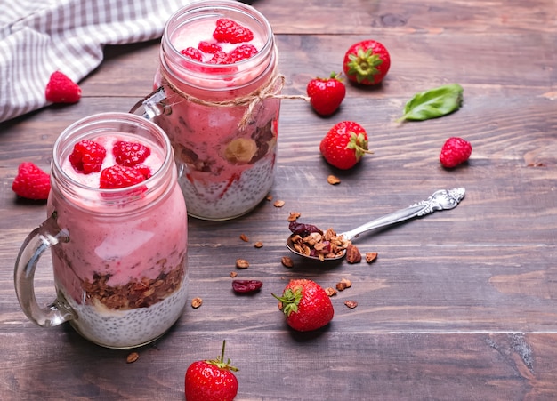 Barattoli per la colazione sana. Budino di Chia con fragole e muesli sul primo piano del tavolo in legno.