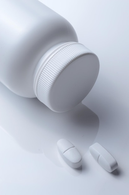 Barattolo di medicina in plastica bianca e due pillole bianche su sfondo chiaro