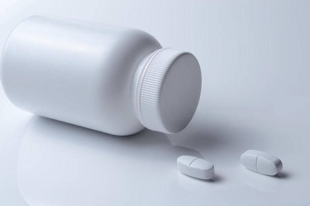 Barattolo di medicina in plastica bianca e due pillole bianche su sfondo chiaro