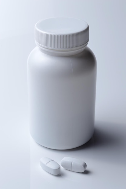 Barattolo di medicina in plastica bianca e due pillole bianche su sfondo chiaro