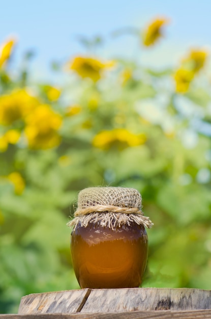 Barattolo di miele e girasoli sulla tavola di legno sopra il giardino del bokeh. Concetto di mangiare sano