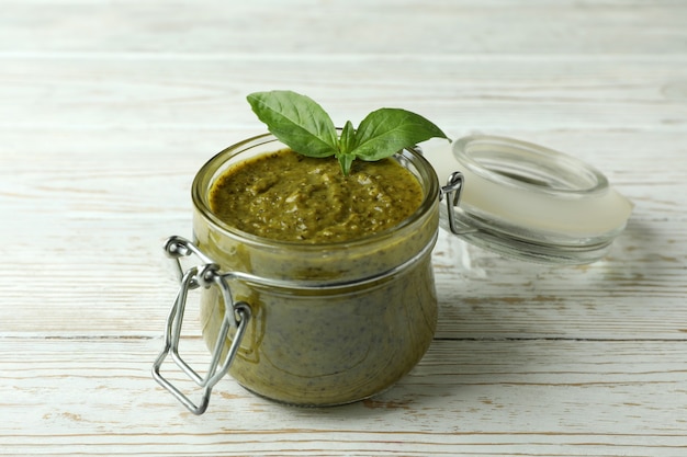 Barattolo di salsa al pesto su fondo di legno bianco