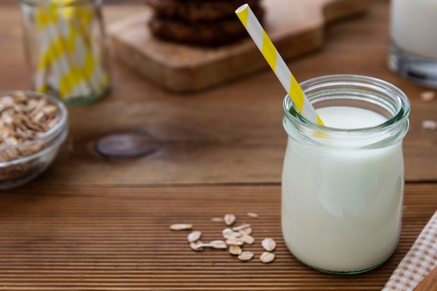 Barattolo di vetro, bottiglia di latte d'avena con paglia di carta su fondo di legno