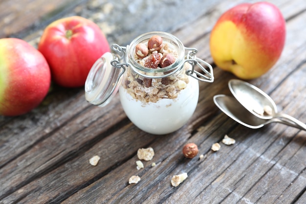 Barattolo di vetro con muesli allo yogurt e mandorle noci Nettarina e mele su sfondo di legno con cucchiai