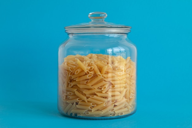 Barattolo di vetro riempito con pasta di penne isolata su fondo blu