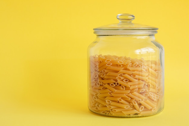 Barattolo di vetro riempito di pasta di penne isolata su fondo giallo