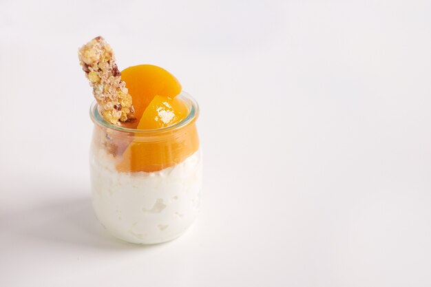 Barattolo di yogurt o cagliata con granola e le albicocche in scatola su fondo bianco, fine