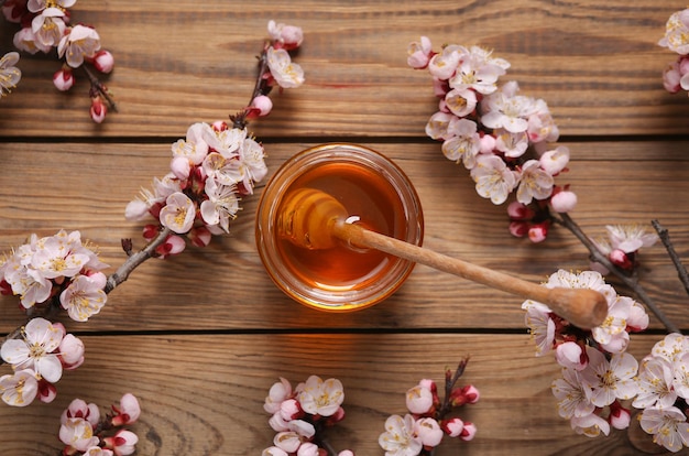 Barattolo Honey Bee con cucchiaio di legno e bellissimo ramo fiorito su sfondo di legno Concetto di primavera