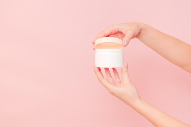Barattolo rotondo di crema cosmetica in mano su sfondo rosa Modello di bellezza cosmetica per il marchio del prodotto