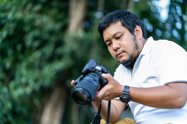 Barba asiatica L'uomo della fotocamera professionale tailandese controlla l'immagine scattata tramite liveview dietro Fotocamera mirrorless di medio formato con sfondo verde albero