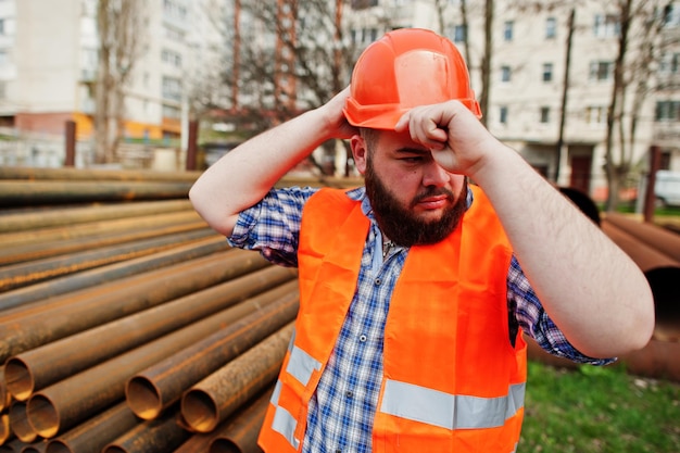 Barba lavoratore uomo vestito operaio edile in casco arancione di sicurezza vicino a tubi d'acciaio