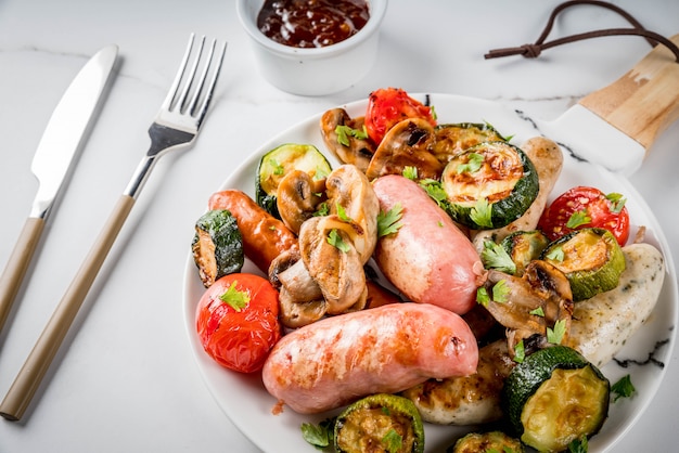 Barbecue. Assortimento di varie salsicce di carne alla griglia, con verdure BBQ funghi, pomodori, zucchine, cipolle. Sul tavolo di marmo bianco, sul piatto, con salsa. copyspace