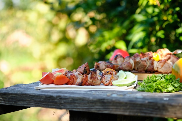 Barbecue e verdure appena cucinate su un tavolo di legno. Pranzo estivo nella natura.