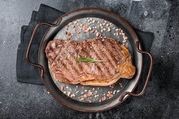 Barbecue Filetto alla griglia o bistecca di carne di manzo di New York con sale rosa ed erbe aromatiche Sfondo nero Vista dall'alto