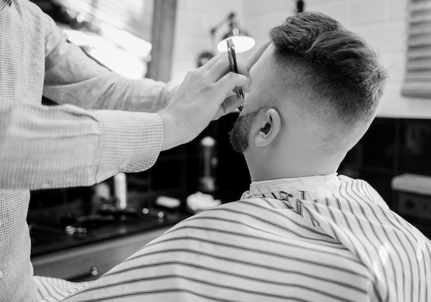 Barber lavora con un rasoio a mano libera con un cliente. un uomo barbuto si fa la barba dal barbiere