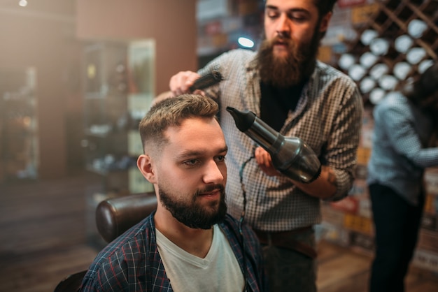 Barbiere asciugare i capelli del cliente con l'asciugacapelli.