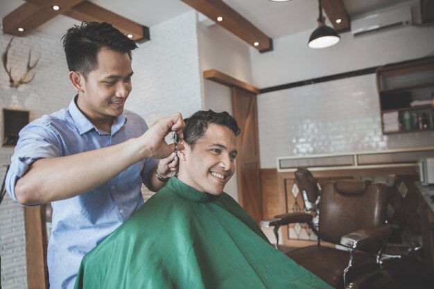 Barbiere che fa taglio di capelli dell'uomo attraente nel negozio di barbiere