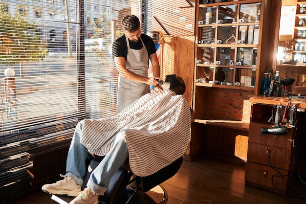 Barbiere che rimuove i peli superflui dalla barba del cliente dopo il taglio