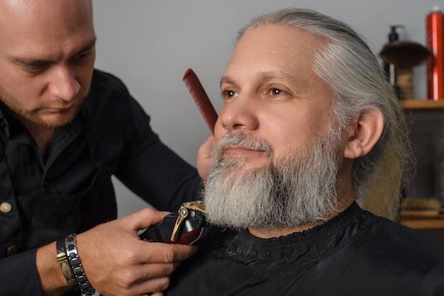 Barbiere che taglia e disegna la barba di un uomo dai capelli grigi B Barbiere per uomo