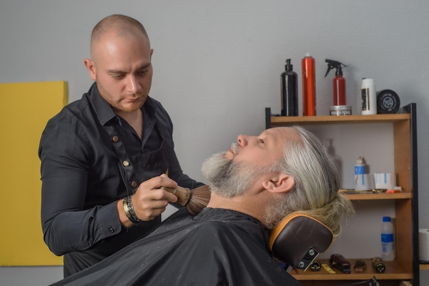 Barbiere che taglia e disegna la barba di un uomo dai capelli grigi B Barbiere per uomo