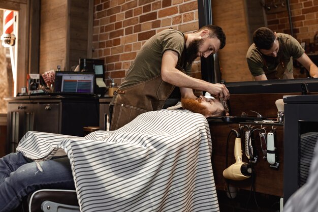 Barbiere e uomo barbuto nel negozio di barbiere