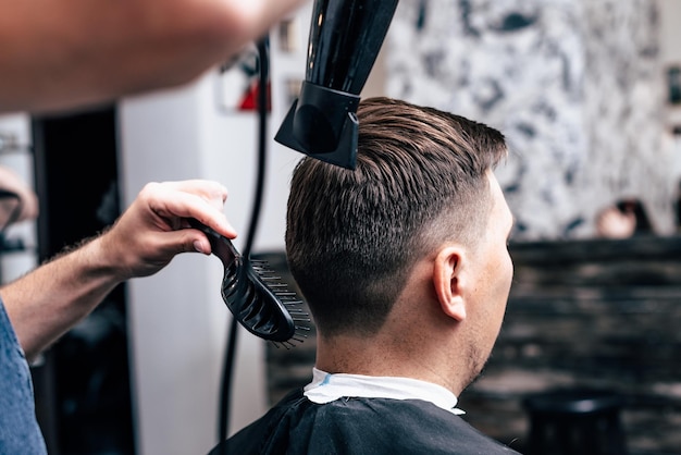 Barbiere in Barbershop taglio auto elettrica per capelli a giovane ragazzo hipper per acconciatura alla moda.