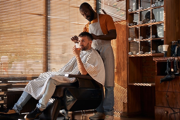 Barbiere in grembiule che taglia i capelli del cliente con le forbici