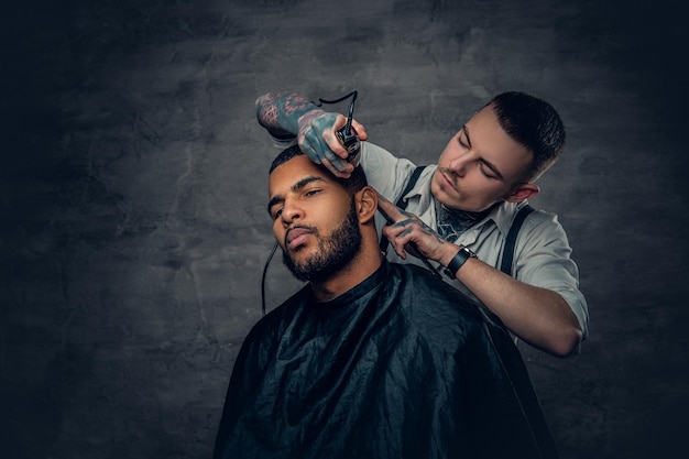 Barbiere maschio caucasico tatuato che taglia la barba all'uomo nero alla moda.