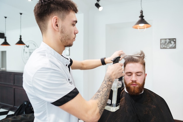 Barbiere maschio che pettina i capelli di un cliente maschio al negozio di barbiere