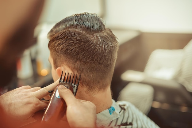 Barbiere. Primo piano del taglio di capelli dell'uomo, il maestro fa lo styling dei capelli nel negozio di barbiere. Foto d'epoca tonica.