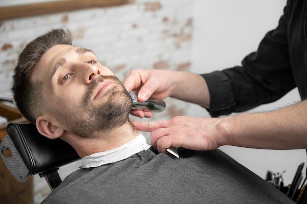 Barbiere professionista che taglia la barba dell'uomo bello Fotografia di alta qualità