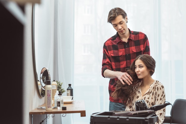 Barbiere stilista che disegna i capelli lunghi per la bella giovane donna asiatica nel momento di lavoro del salone di bellezza