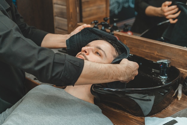 Barbiere, un uomo si lava i capelli. Barber lava il suo cliente. Lavare i capelli e le barbe dopo il taglio. Cura personale