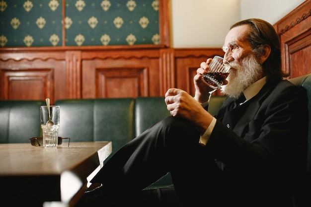 Barbuto anziano uomo d'affari. L'uomo beve un whisky. Senior in abito nero.