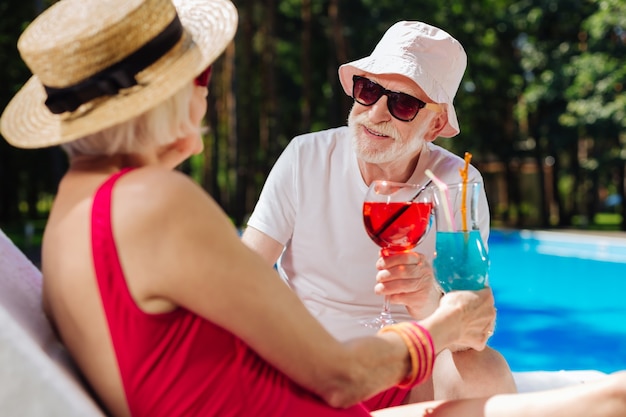 Barbuto pensionato uomo che indossa cappello estivo e occhiali da sole guardando la sua bella moglie moderna