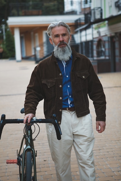 Barbuto uomo maturo che indossa giacca alla moda a piedi con la sua bicicletta