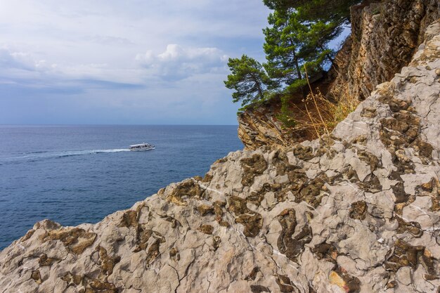 Barca bianca e scogliera rocciosa con pini sul mare turchese