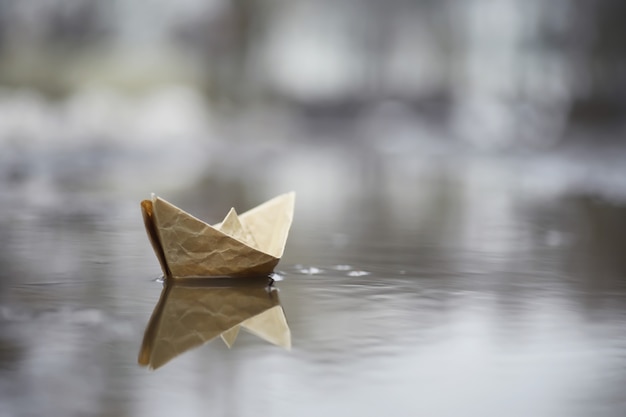 Barca di carta nell'acqua per strada. Il concetto di inizio primavera. Neve che si scioglie e una barca di origami sulle onde dell'acqua.