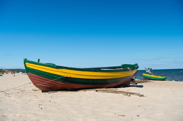 Barca o nave, moderna imbarcazione marina con vernice colorata all'ormeggio sulla spiaggia sabbiosa soleggiata all'aperto su sfondo blu del cielo e del mare