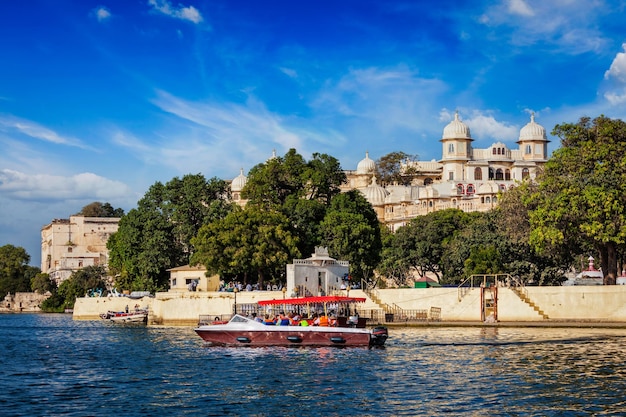 Barca toruista sul lago pichola con il palazzo della città sullo sfondo udaipur india